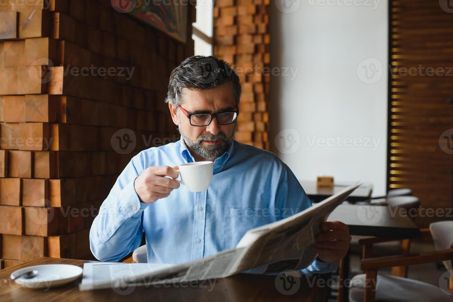 Closeup portrait of serious senior handsome man reading newspaper, having coffee break and sitting at table. photo