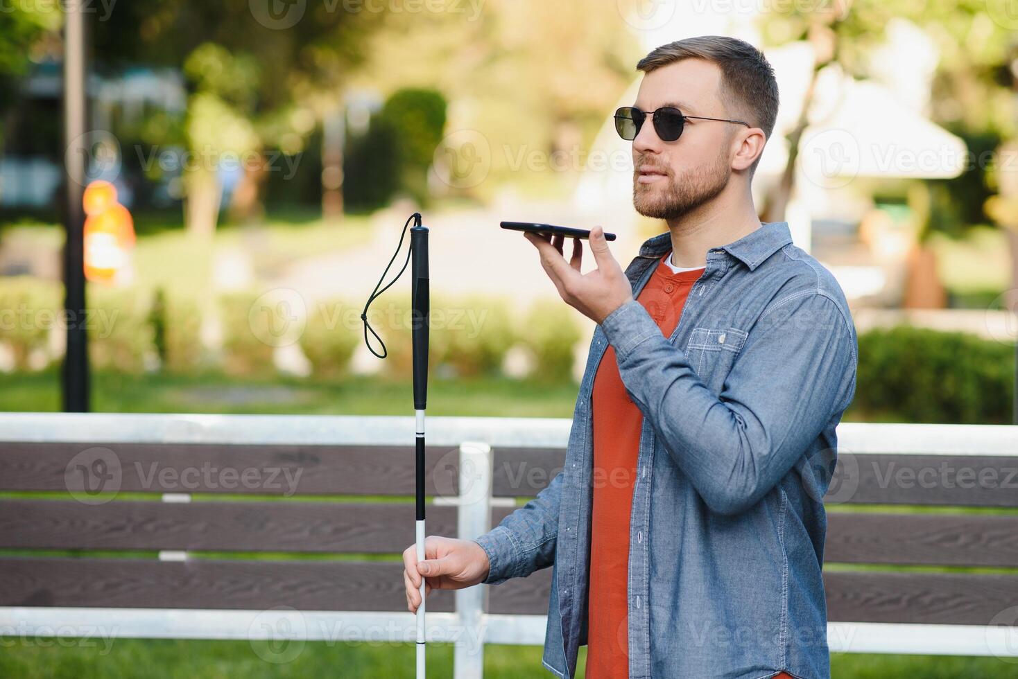 Young blinded man using phone and sending voice message photo