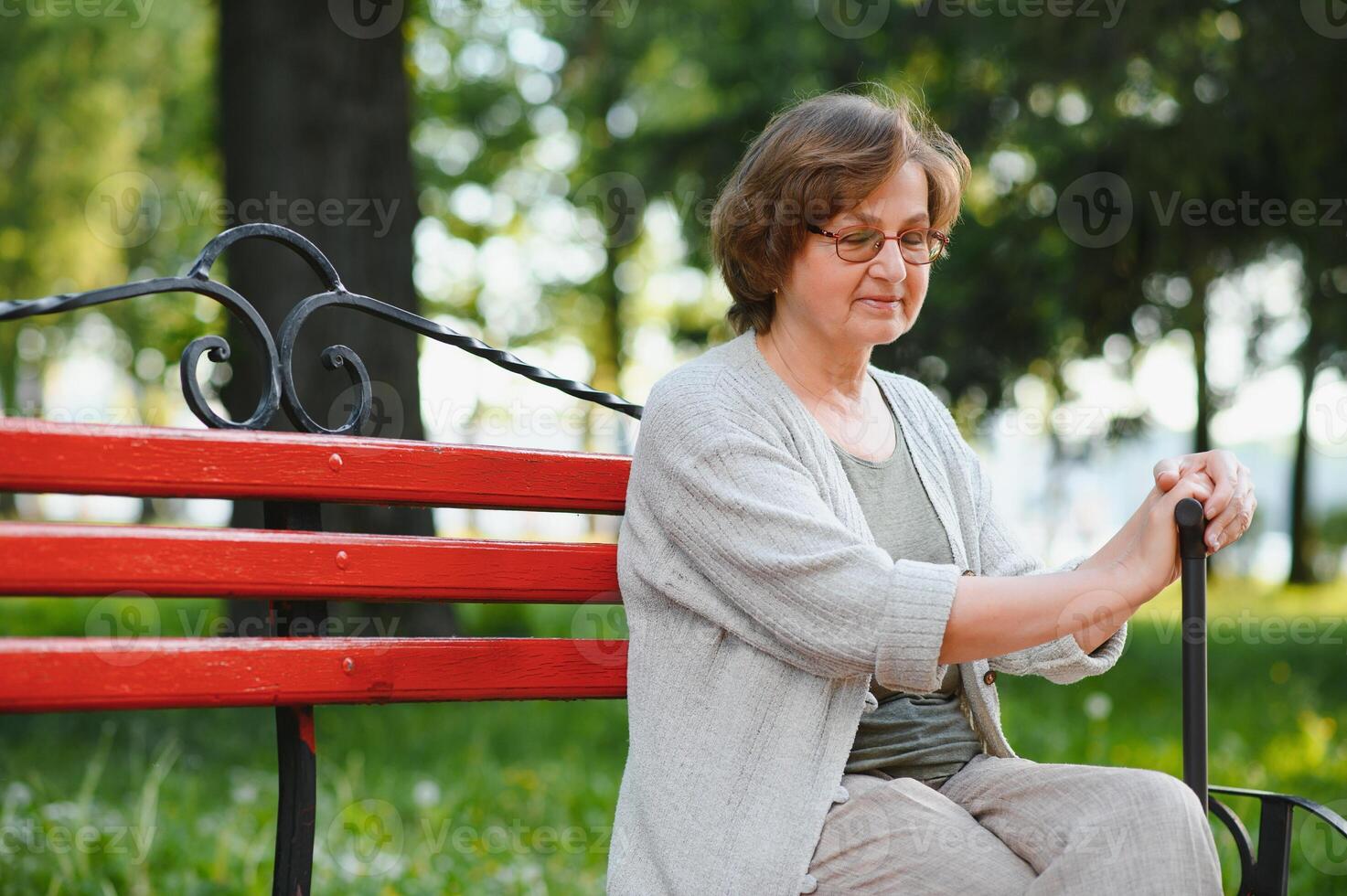 An elderly woman sitting on bench in summer park photo