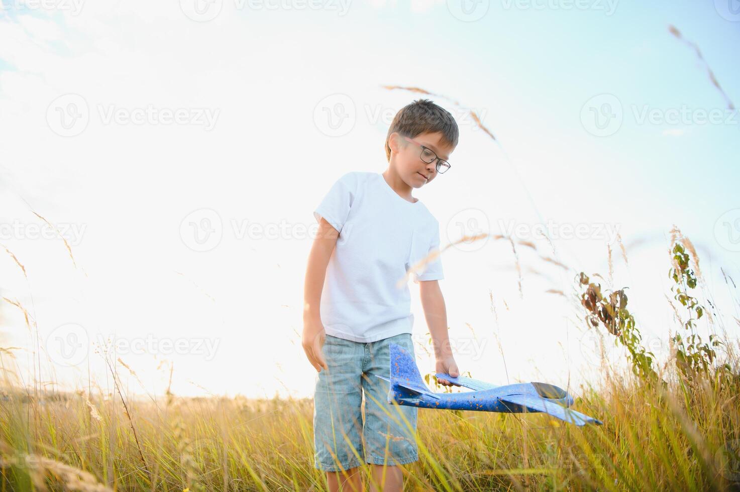 Cute happy cheerful child running fastly along grassy hill at countryside holding big toy plane in hand. Boy playing during sunset time in evening. Horizontal color photography. photo