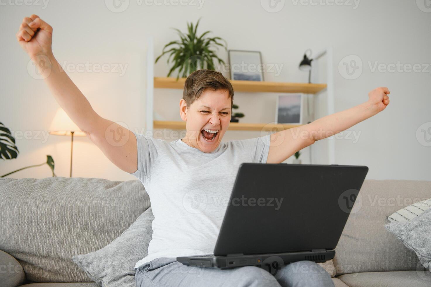 Excited mature woman looking at laptop screen, reading good news in message, celebrating online lottery win, rejoicing success, overjoyed older female sitting on couch at home, using computer. photo