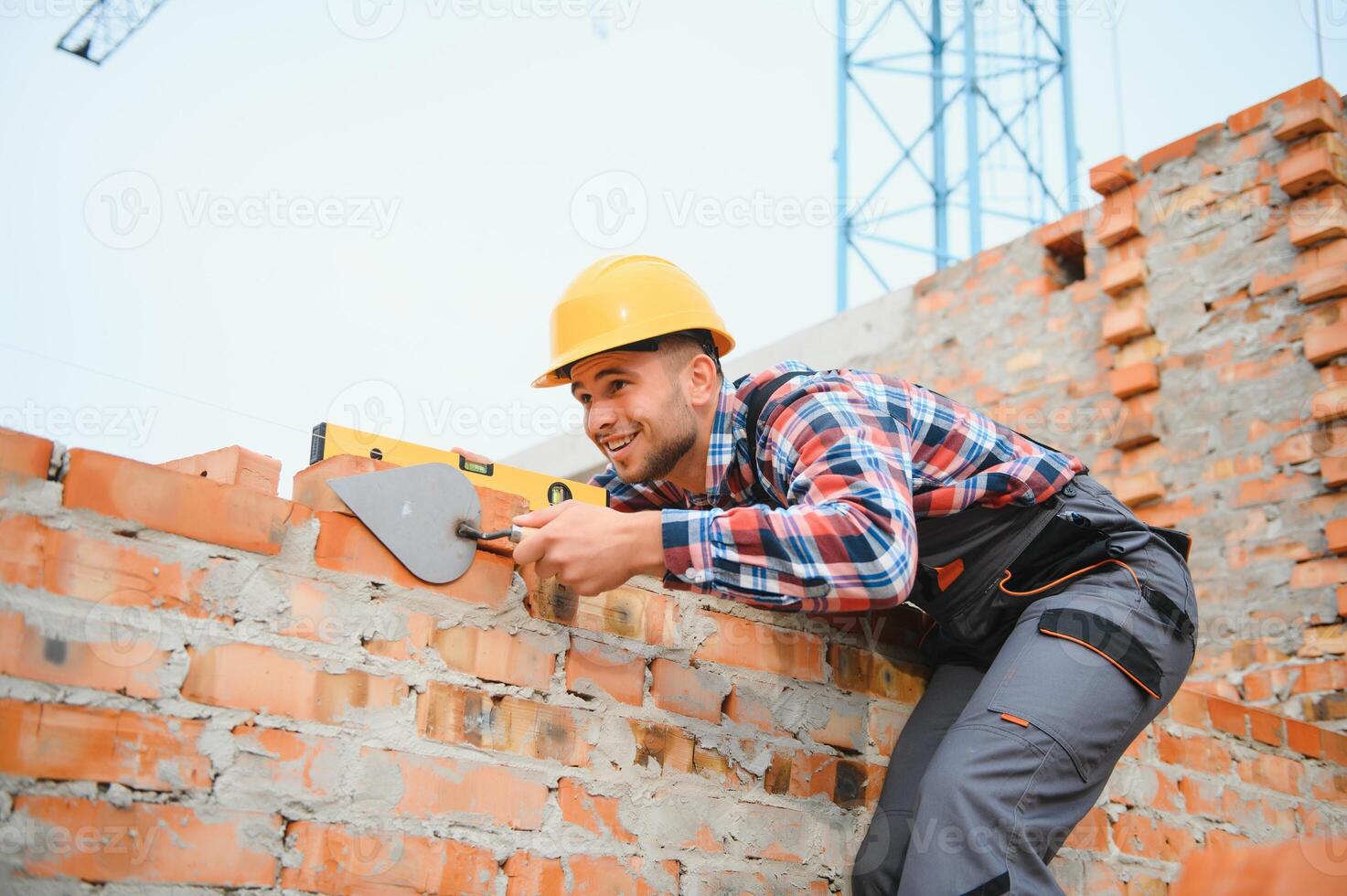 Using bricks. Young construction worker in uniform is busy at the unfinished building photo