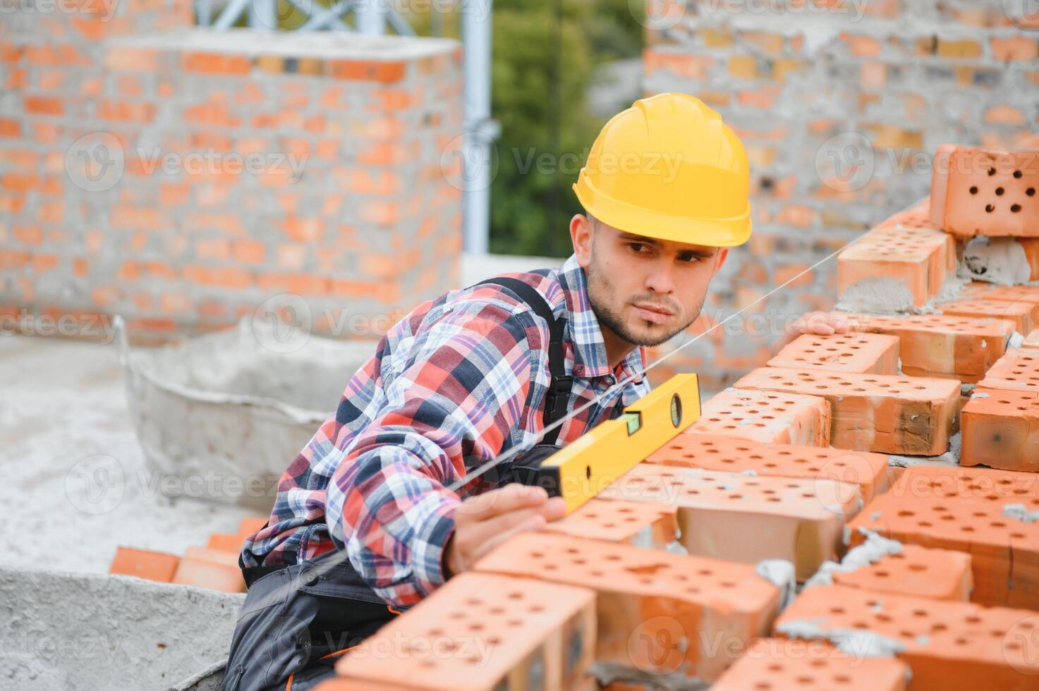 Using bricks. Young construction worker in uniform is busy at the unfinished building photo