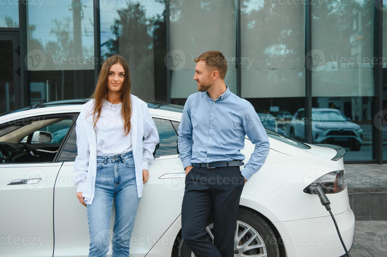 Smiling man and woman on the charging station for electric cars. A man is charging a car. photo