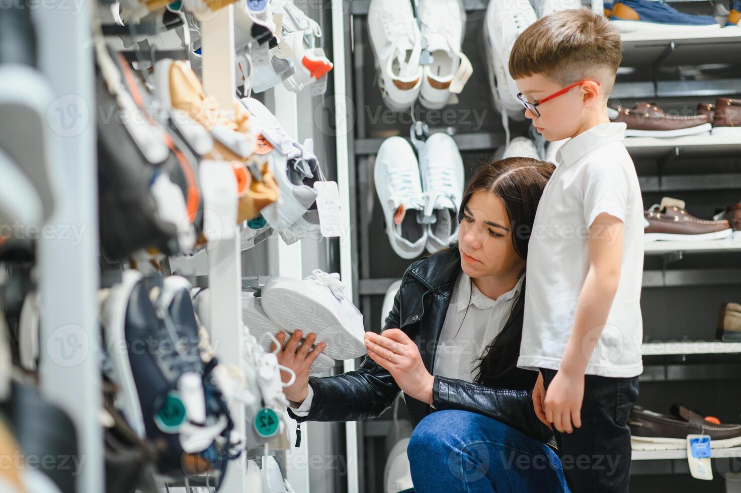 woman with child choosing and trying on new boots in shopping mall photo