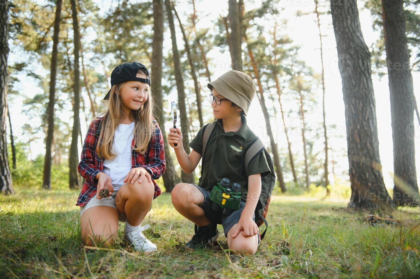 Two kids in casual clothes in exploring nature in forest together during school camping trip with magnifying glass. photo