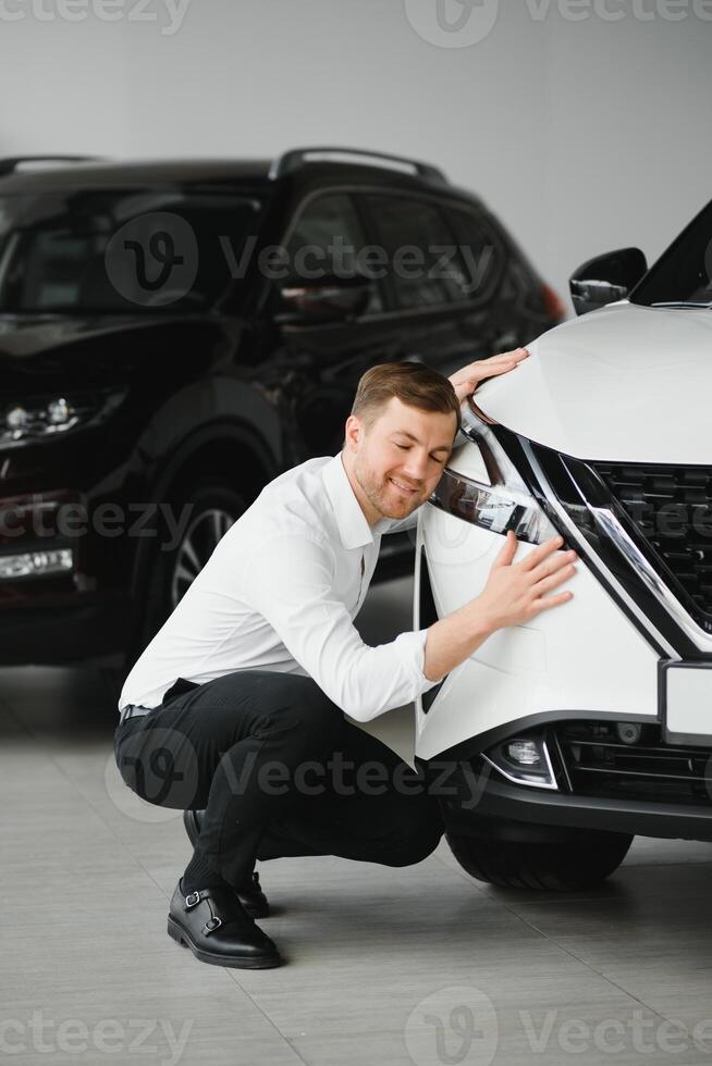 Visiting car dealership. Handsome bearded man is stroking his new car and smiling. photo