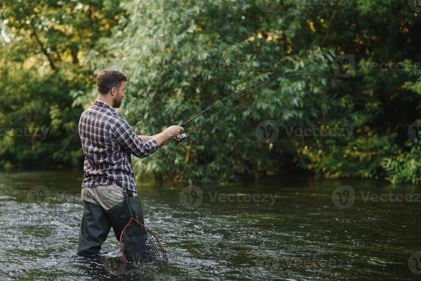 Fisherman catches a trout on the river in summer photo