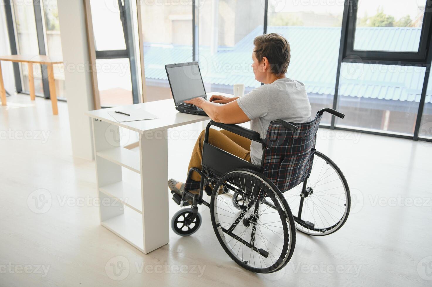 medio años mujer utilizando ordenador portátil sentado en silla de ruedas a hogar foto