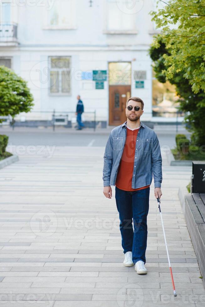 Young handsome blinded man walking with stick in town photo