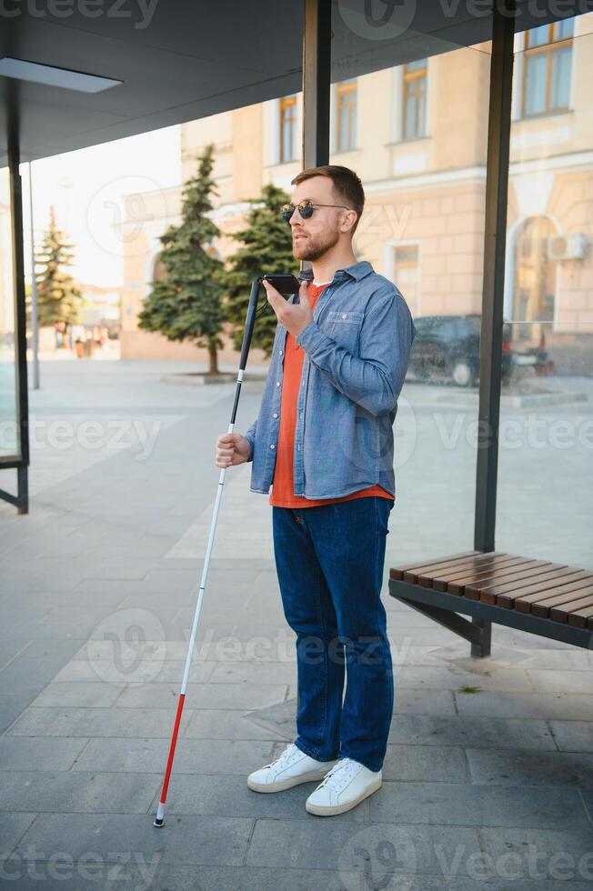 blind man with white cane waiting for public transport in city. photo