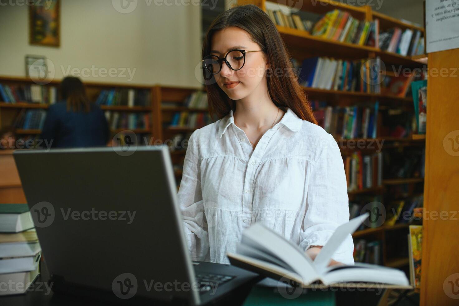 University Library Beautiful Smart Caucasian Girl uses Laptop, Writes Notes for Paper, Essay, Study for Class Assignment. Focused Students Learning, Studying for College Exams. Side View Portrait photo