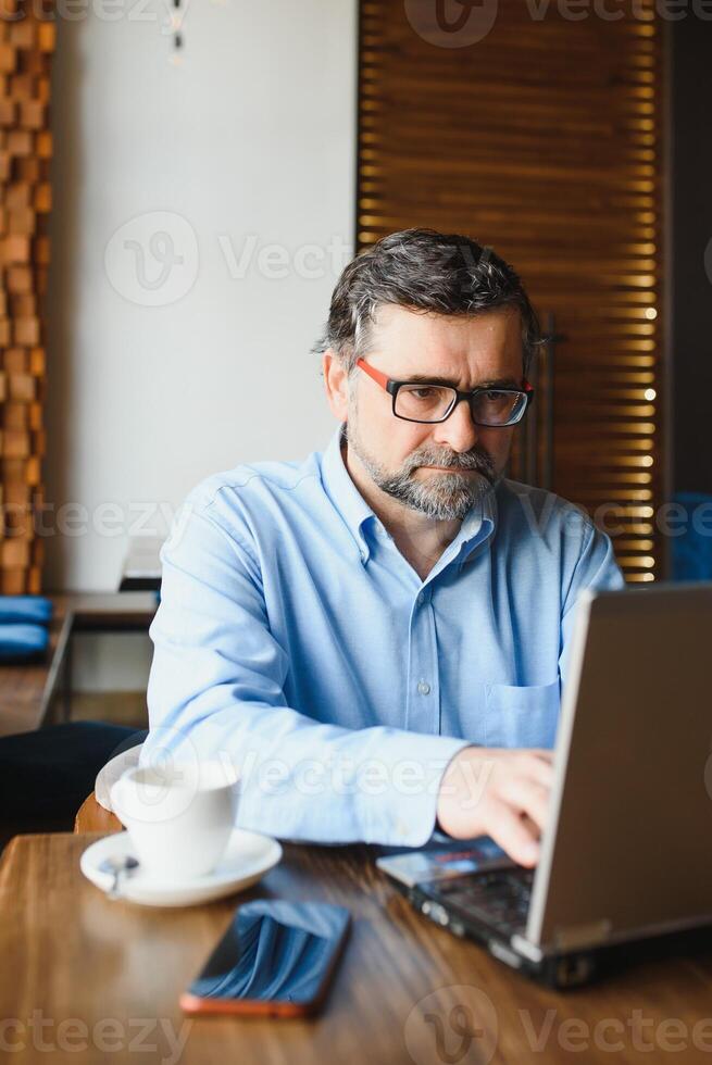 Business, technology and people concept , senior businessman with laptop computer drinking coffee at modern cafe. photo