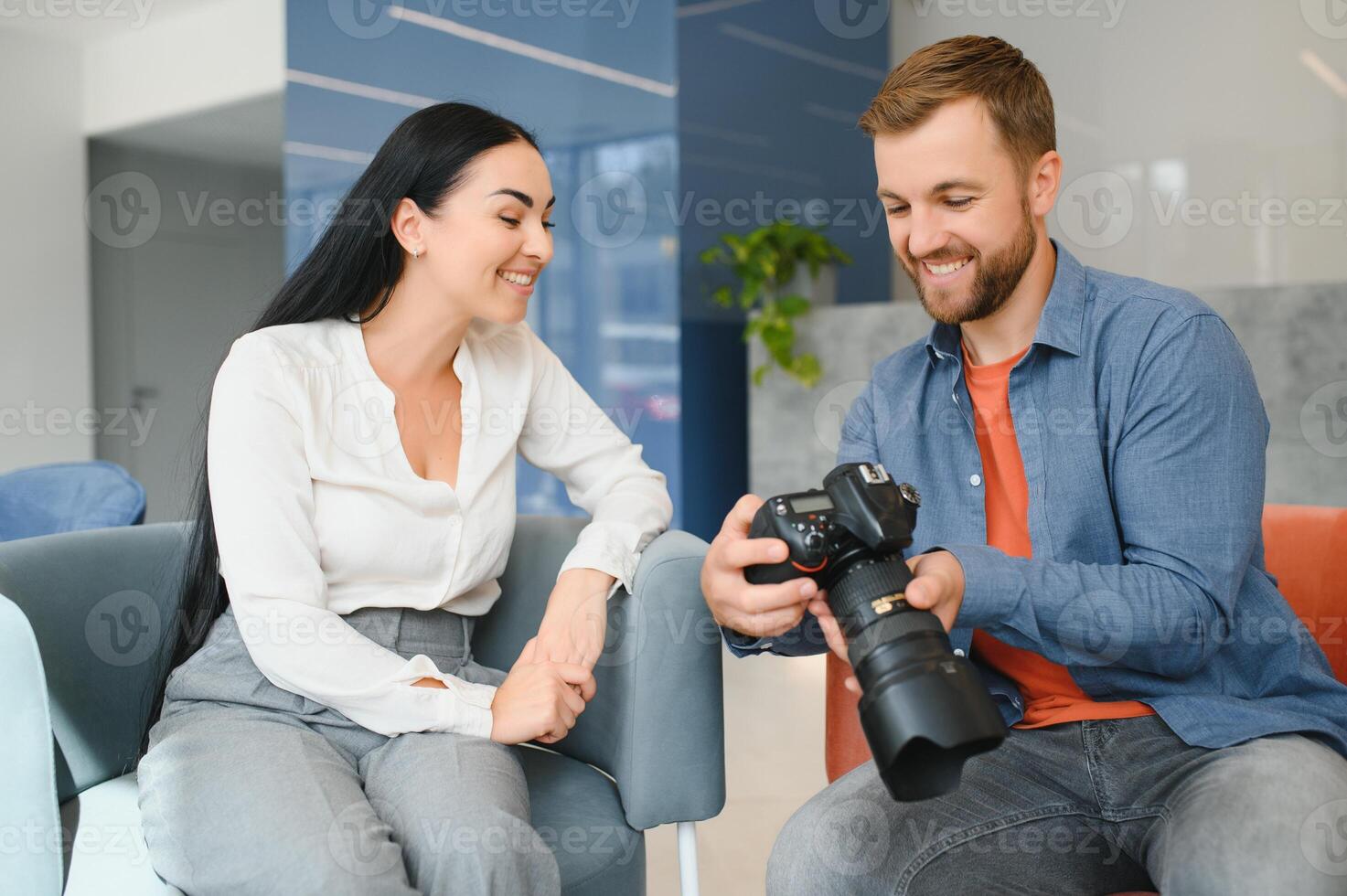 Young photographer man in blue shirt watching photo with client woman after photo session and smiling and looking at each other