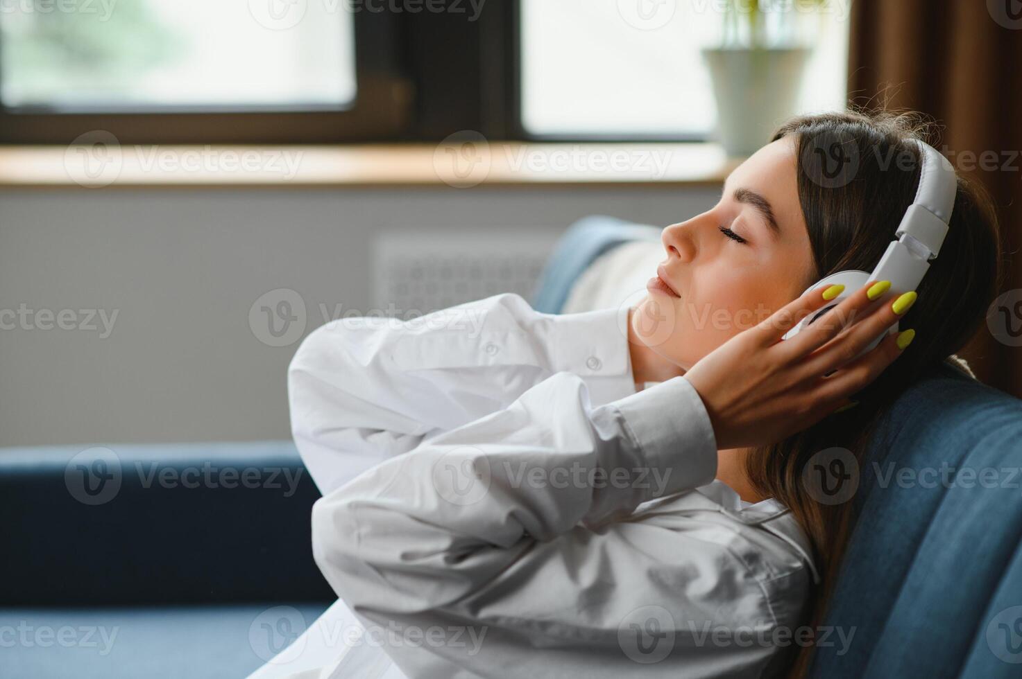 woman sitting on the couch at home listening to music on headphones technologies photo
