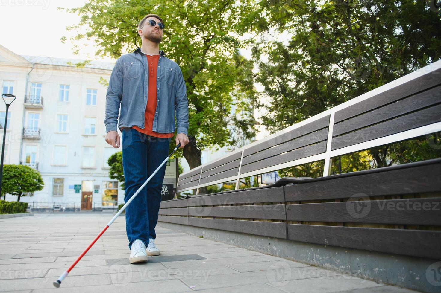 Young handsome blinded man walking with stick in town photo