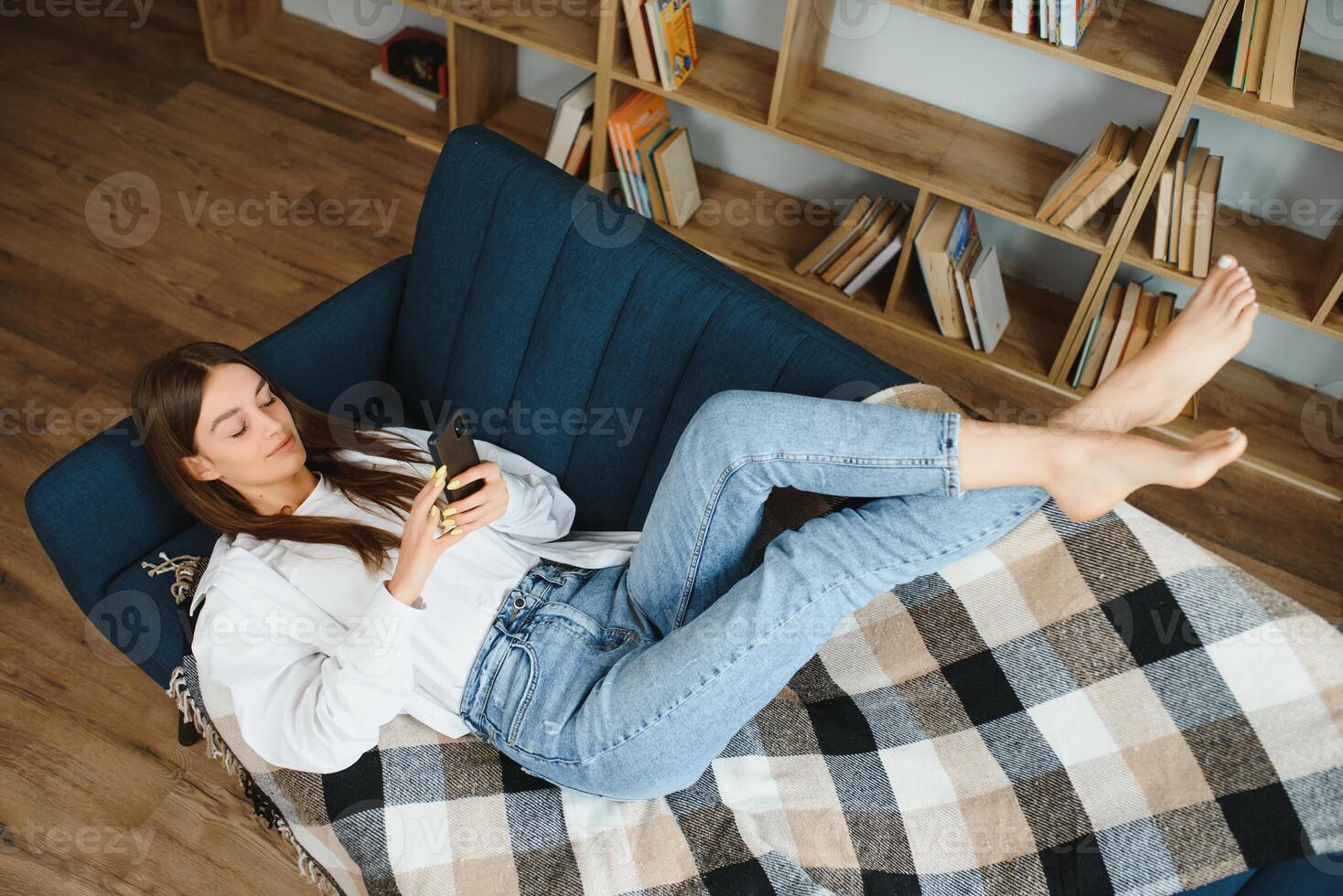 Young beautiful woman wearing white t-shirt on textile sofa at home. Attractive slim female in domestic situation, resting on couch in her lofty apartment. Background, copy space, close up. photo