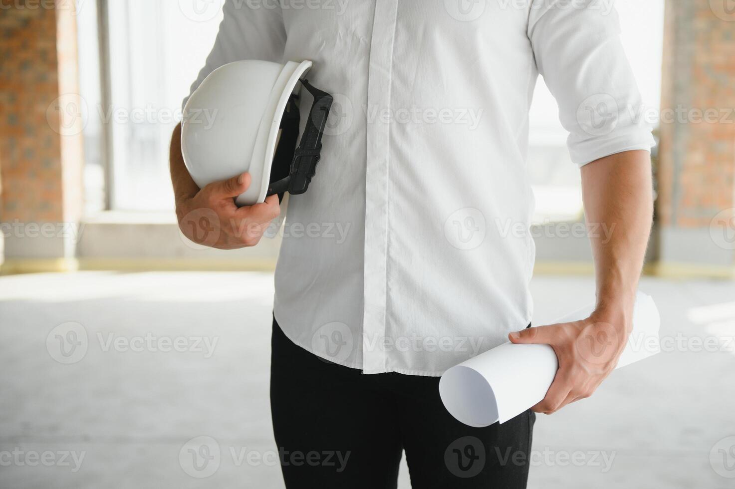 engineer hand holding white safety hat and paper plan blueprint on wood table in working construction site housing building with copy space add text. photo