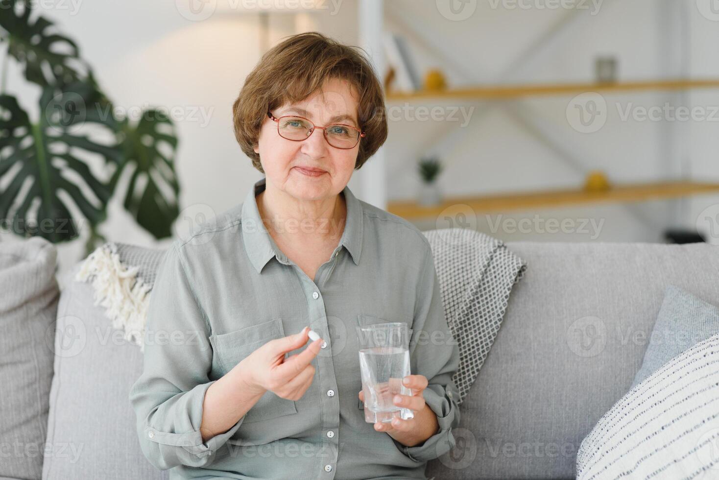 Mature senior middle aged woman holding pill and glass of water taking painkiller to relieve pain, medicine supplements vitamins, antibiotic medication, meds for old person concept, close up view. photo