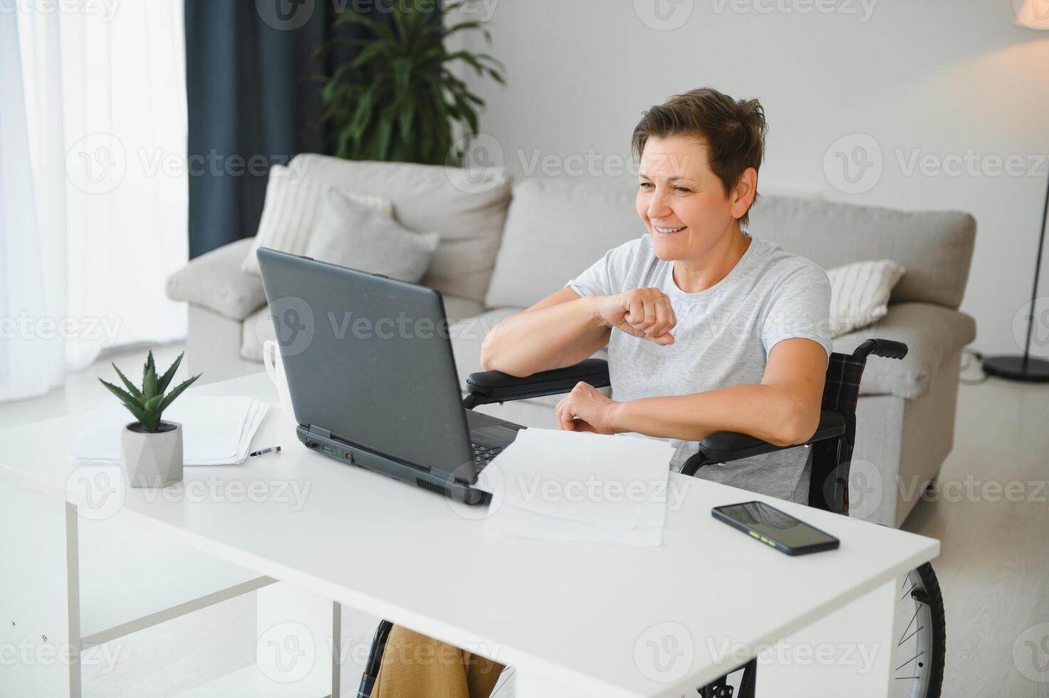Positive elderly woman in wheelchair working on laptop, IT freelancer, online photo