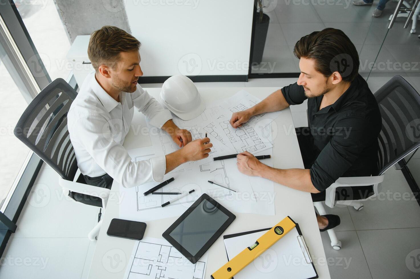 Two engineering working together and using digital tablet looking blueprint and analysis with architectural plan on desk photo