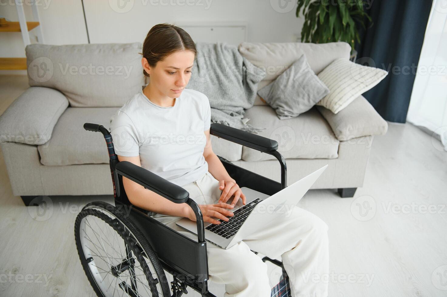 woman in a wheelchair works on the laptop PC in the home office with an assistance dog as a companion photo