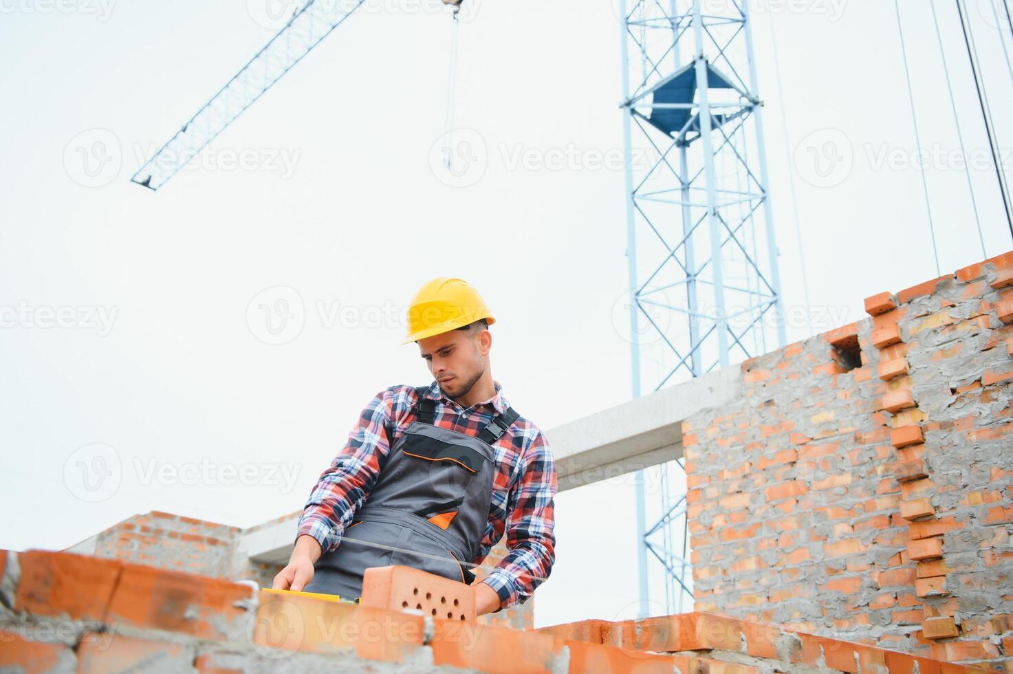 Using bricks. Young construction worker in uniform is busy at the unfinished building photo