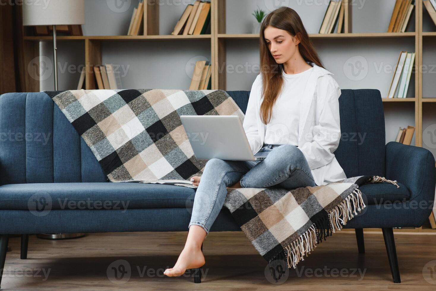 sonriente atractivo joven mujer sentado en sofá utilizando ordenador portátil comunicado trabajando en línea a hogar, contento adolescente niña mecanografía en computadora, disfrutando escritura Blog o chateando con amigos en social red foto