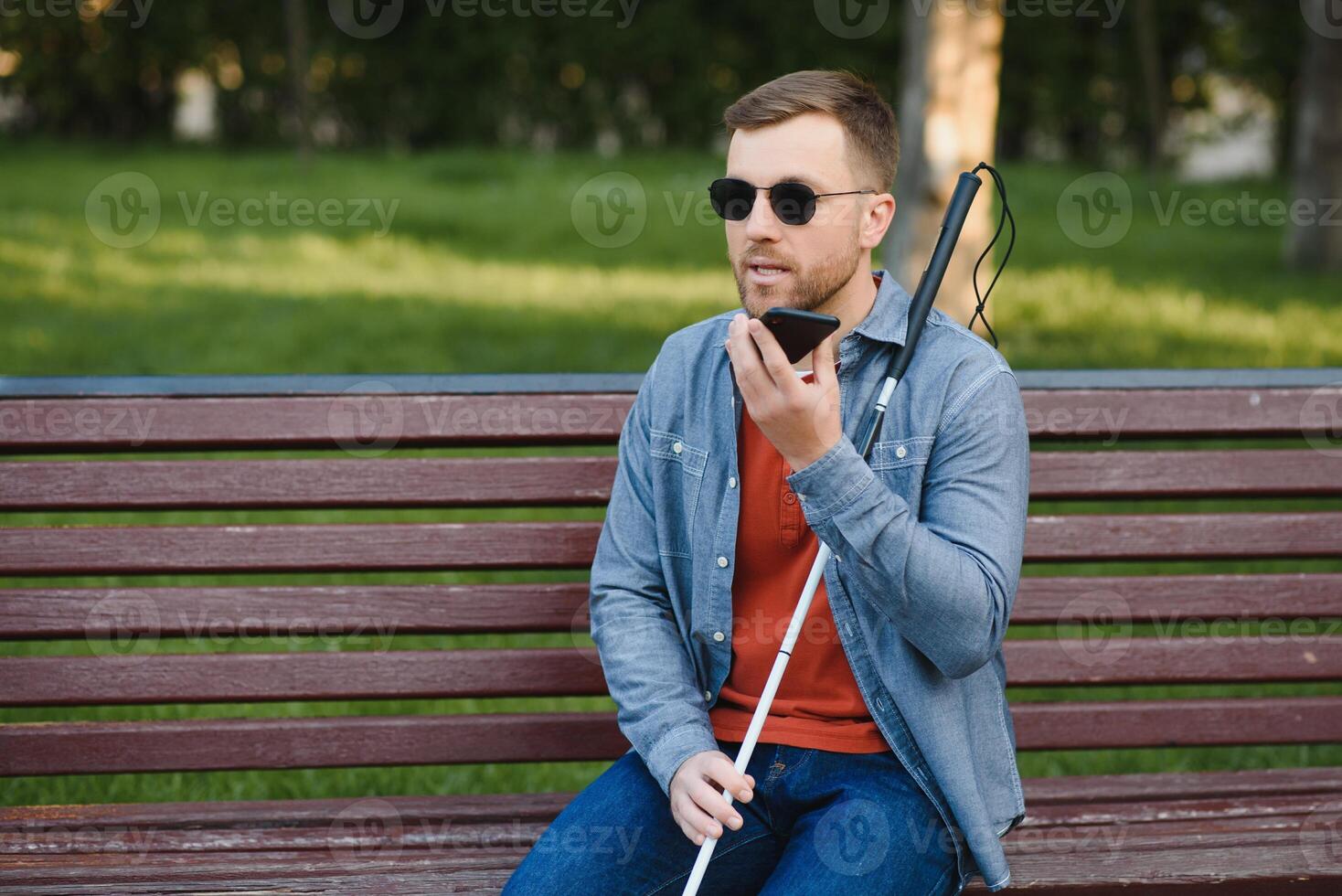 Young blinded man using phone and sending voice message photo