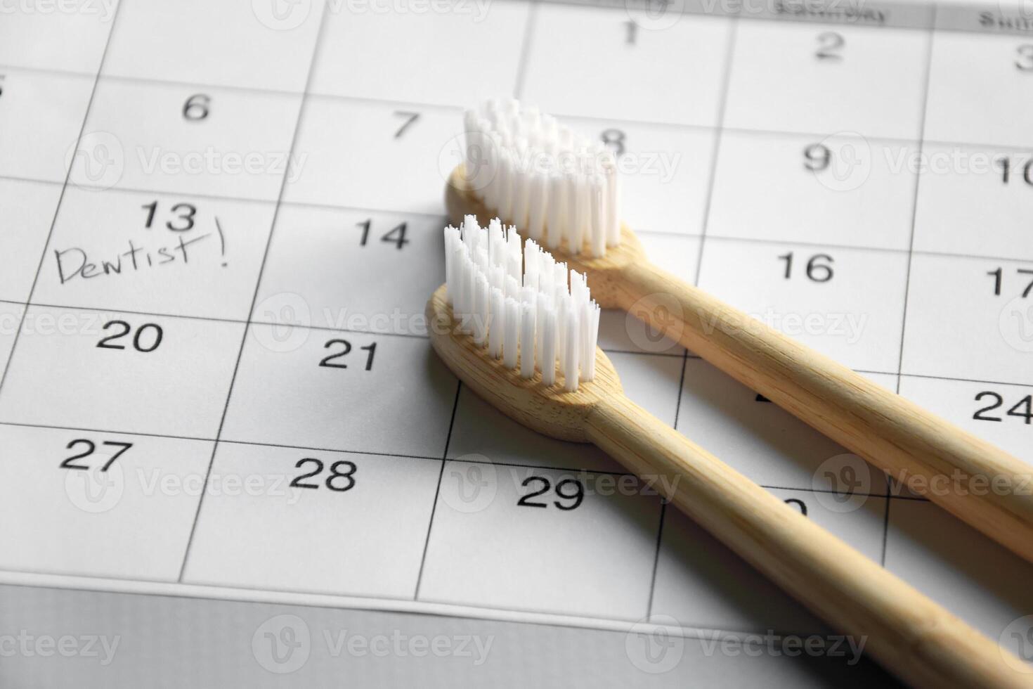 On a light gray background, there is a calendar with a dentist's note and toothbrushes. photo