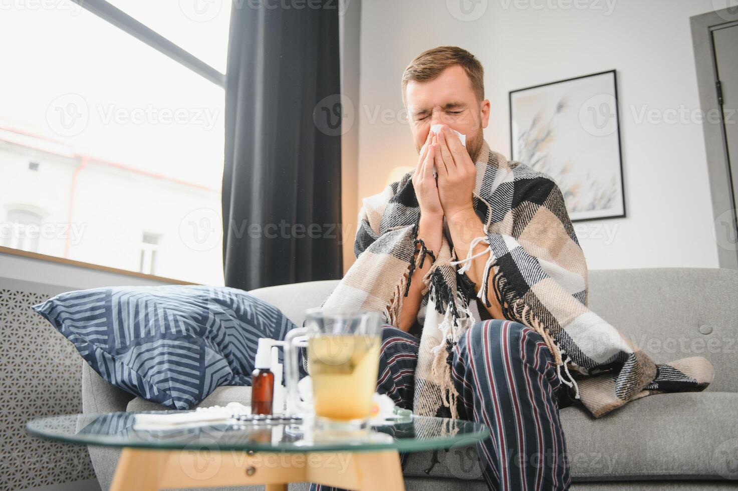 Sick man on sofa at home and blowing nose photo