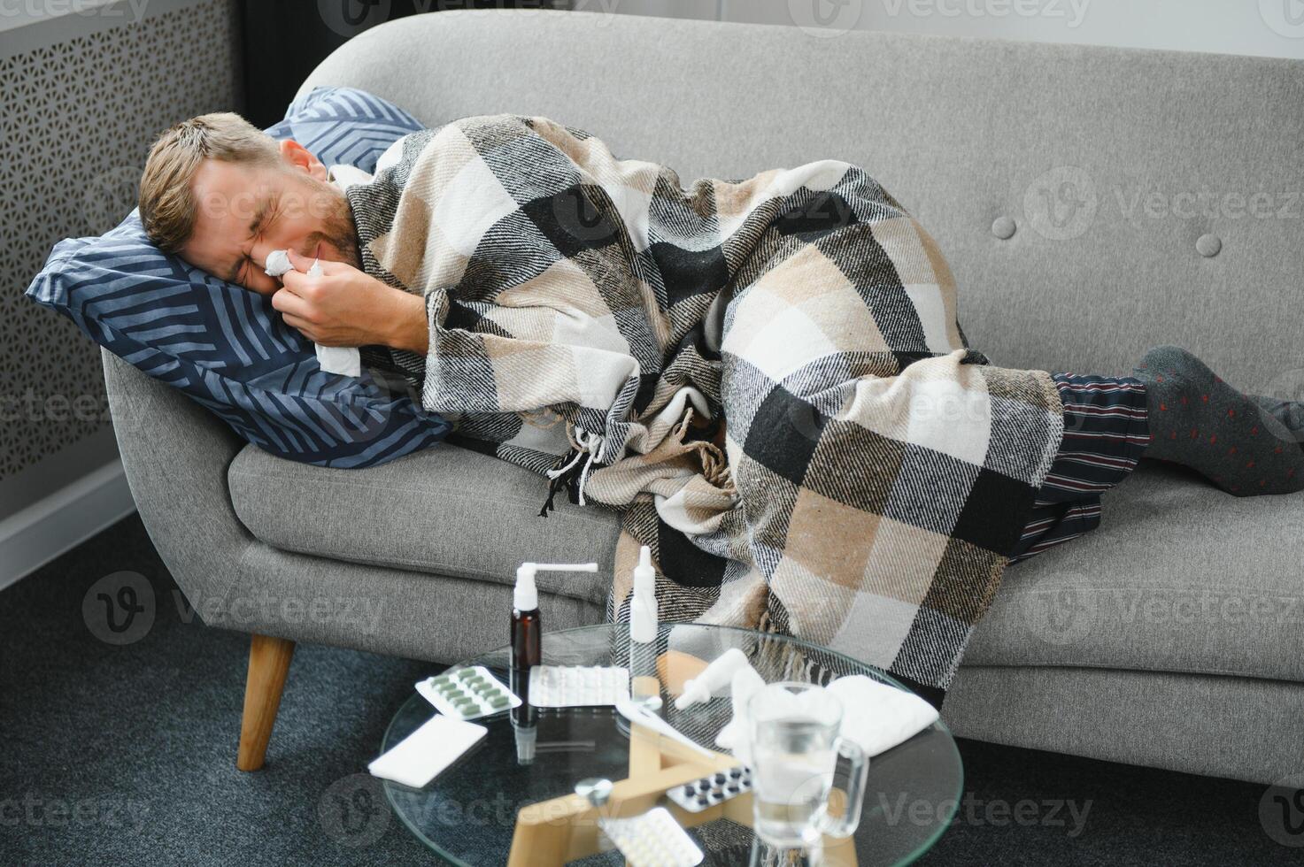 It's cold at home in wintertime. Man freezing in his house in winter because of broken thermostat. young guy wrapped in woolen plaid shivering while sitting on sofa in living room interior photo