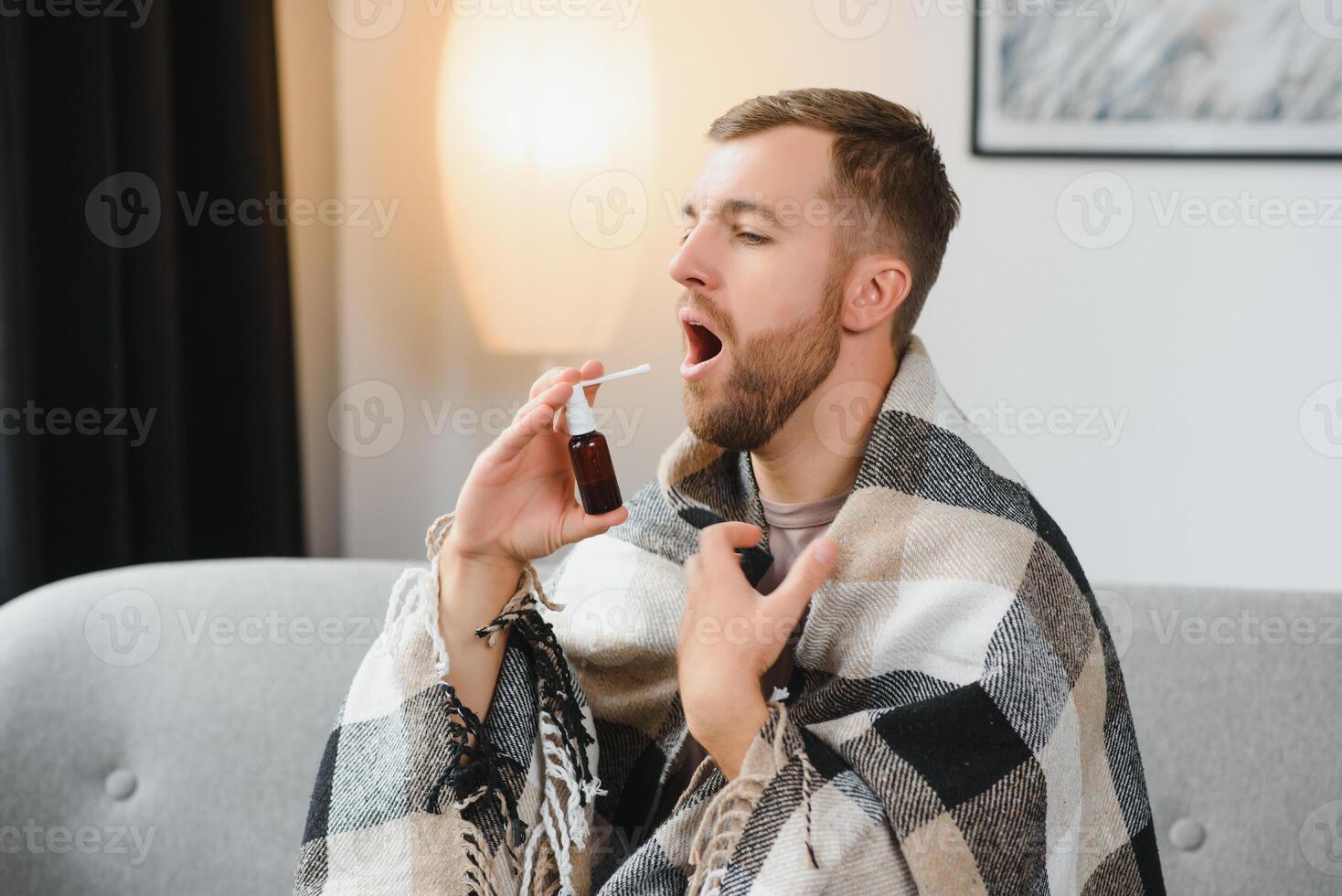 rhinitis, medicine and healthcare concept - sick man in blanket using oral spray at home photo
