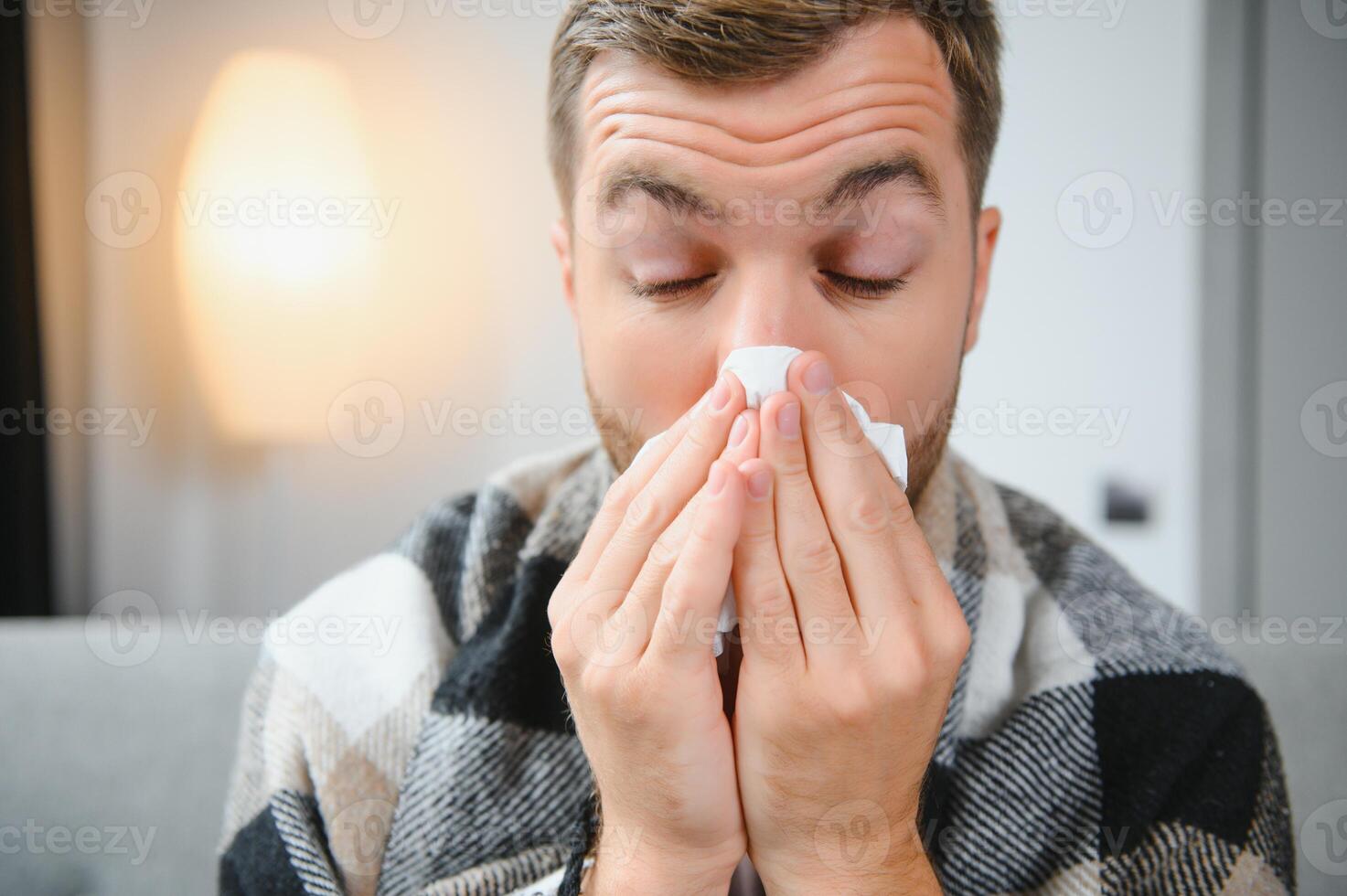 Sick man on sofa at home and blowing nose photo