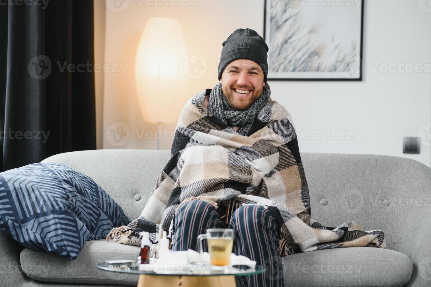 It's cold at home in wintertime. Man freezing in his house in winter because of broken thermostat. young guy wrapped in woolen plaid shivering while sitting on sofa in living room interior photo