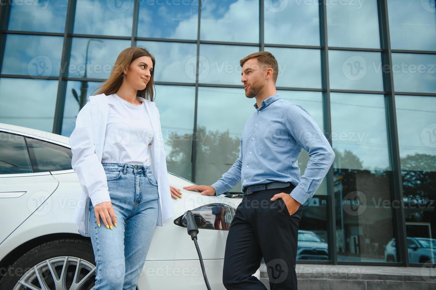 Young couple man and woman traveling together by new car having stop at charging station. photo