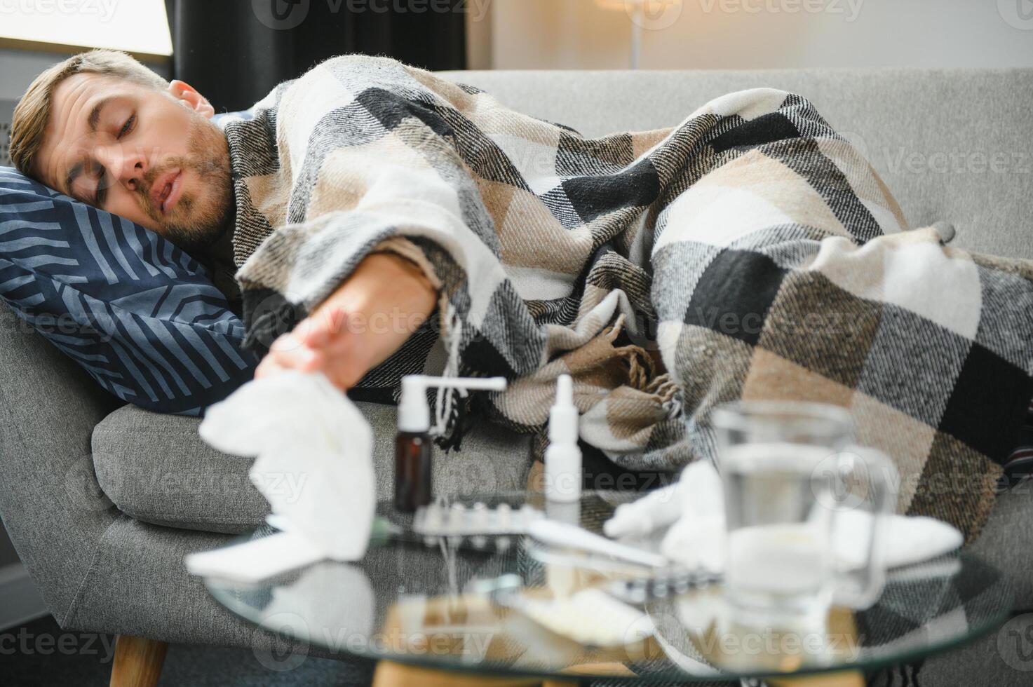 Young man suffering from a common cold and flu or allergy sit at home wrapped in blanket and wipe his nose with tissues while he have a strong headache pain, healthcare concept. photo