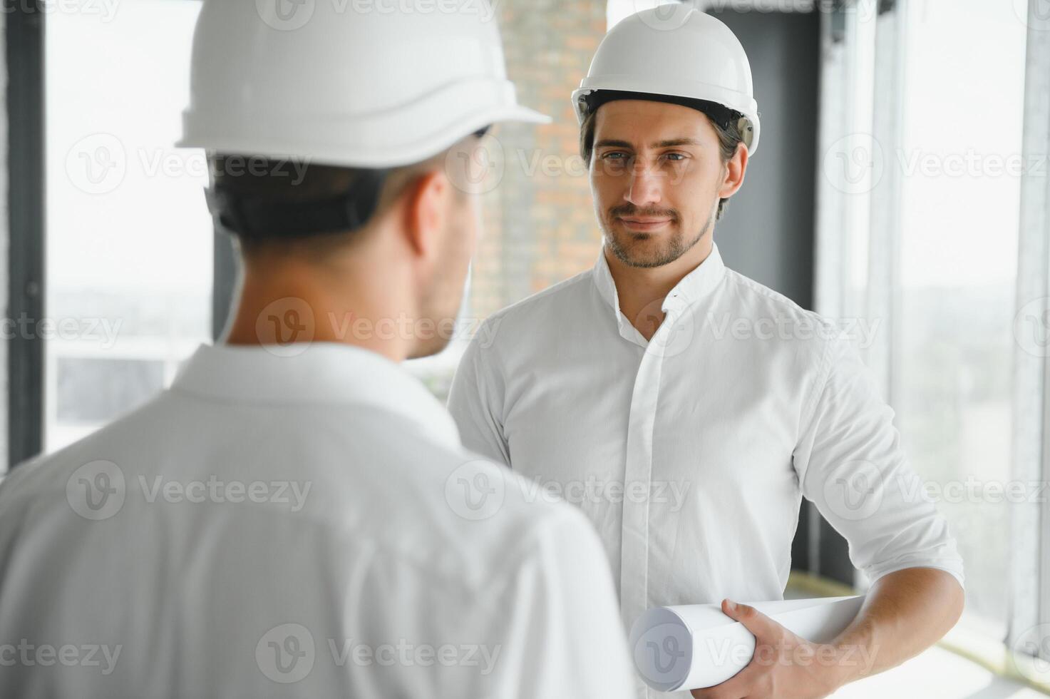 A front view of two smart architects with white helmets reviewing blueprints at a construction site on a bright sunny day photo