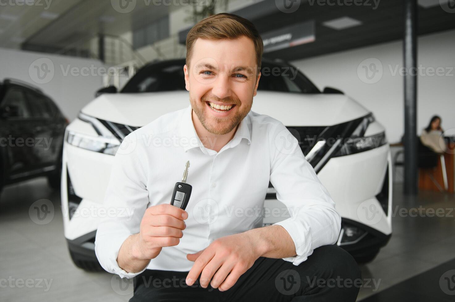 Happy buyer holding keys near the car in front of the modern avtosalon building photo