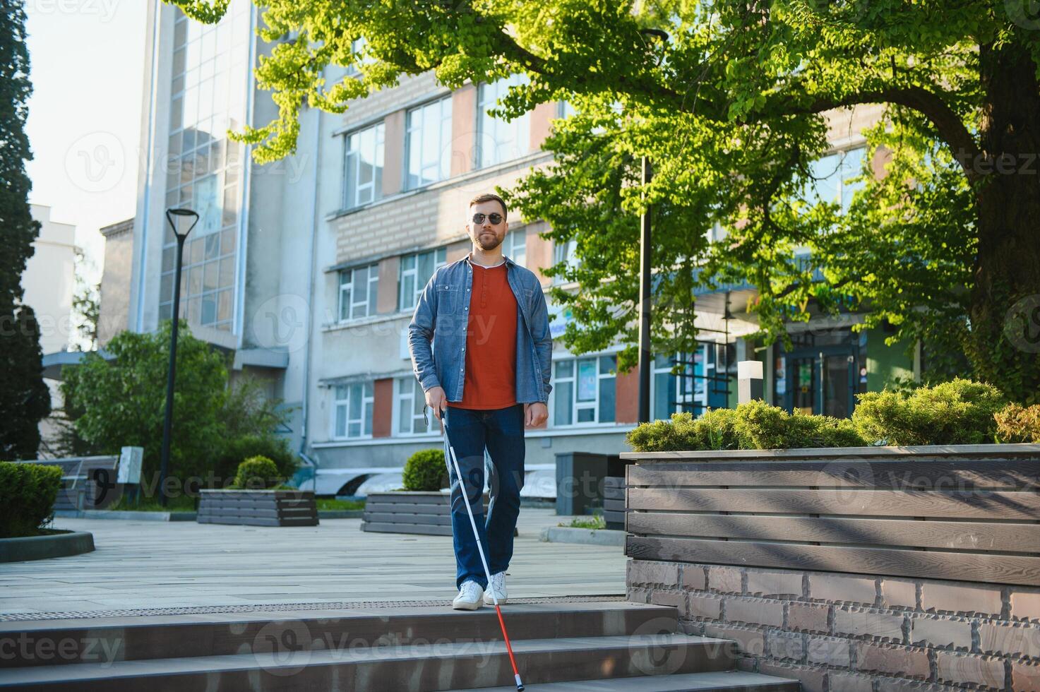 Young handsome blinded man walking with stick in town photo