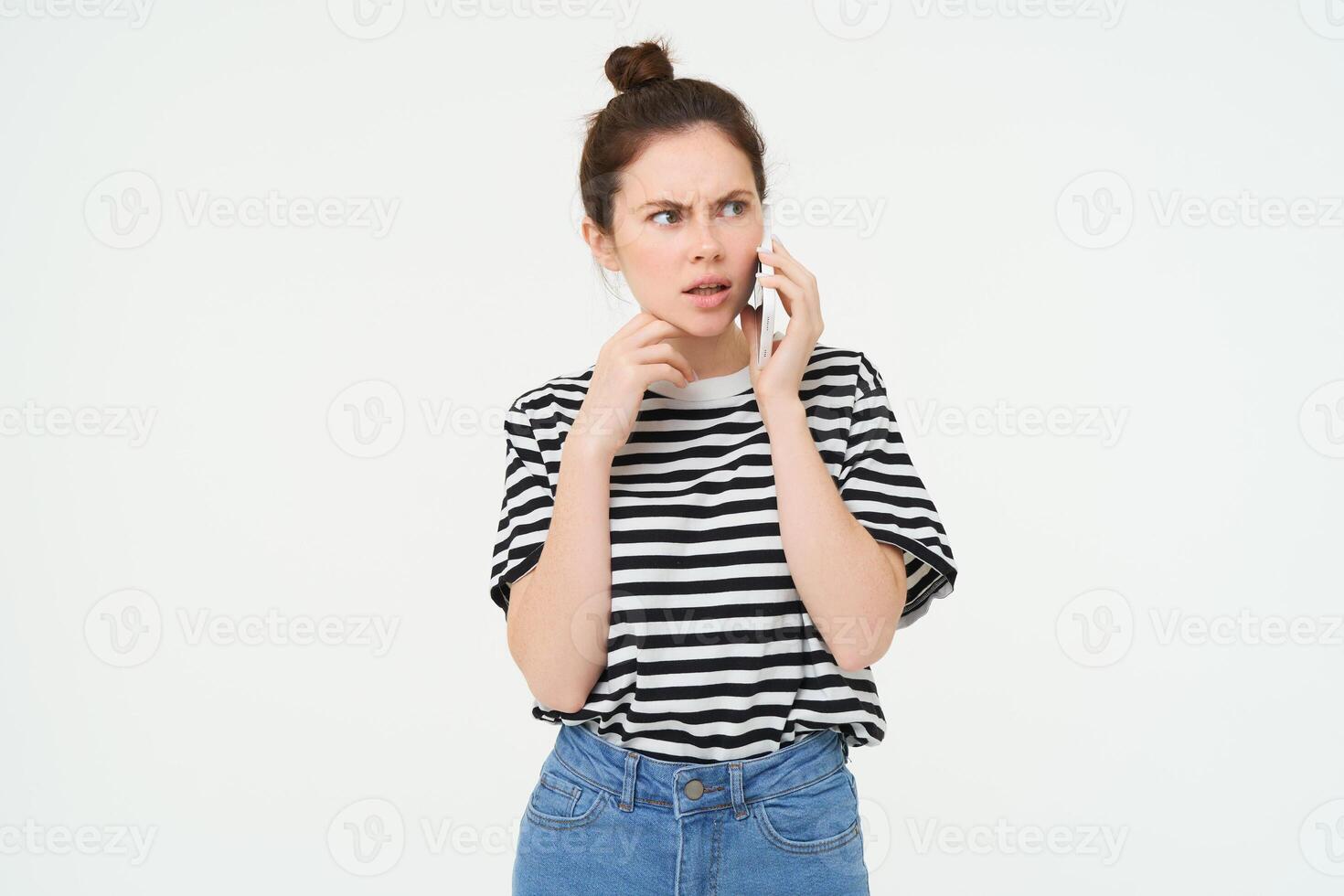 Image of woman with shocked face, looks confused while chats over the phone, listens to person on telephone, white background photo