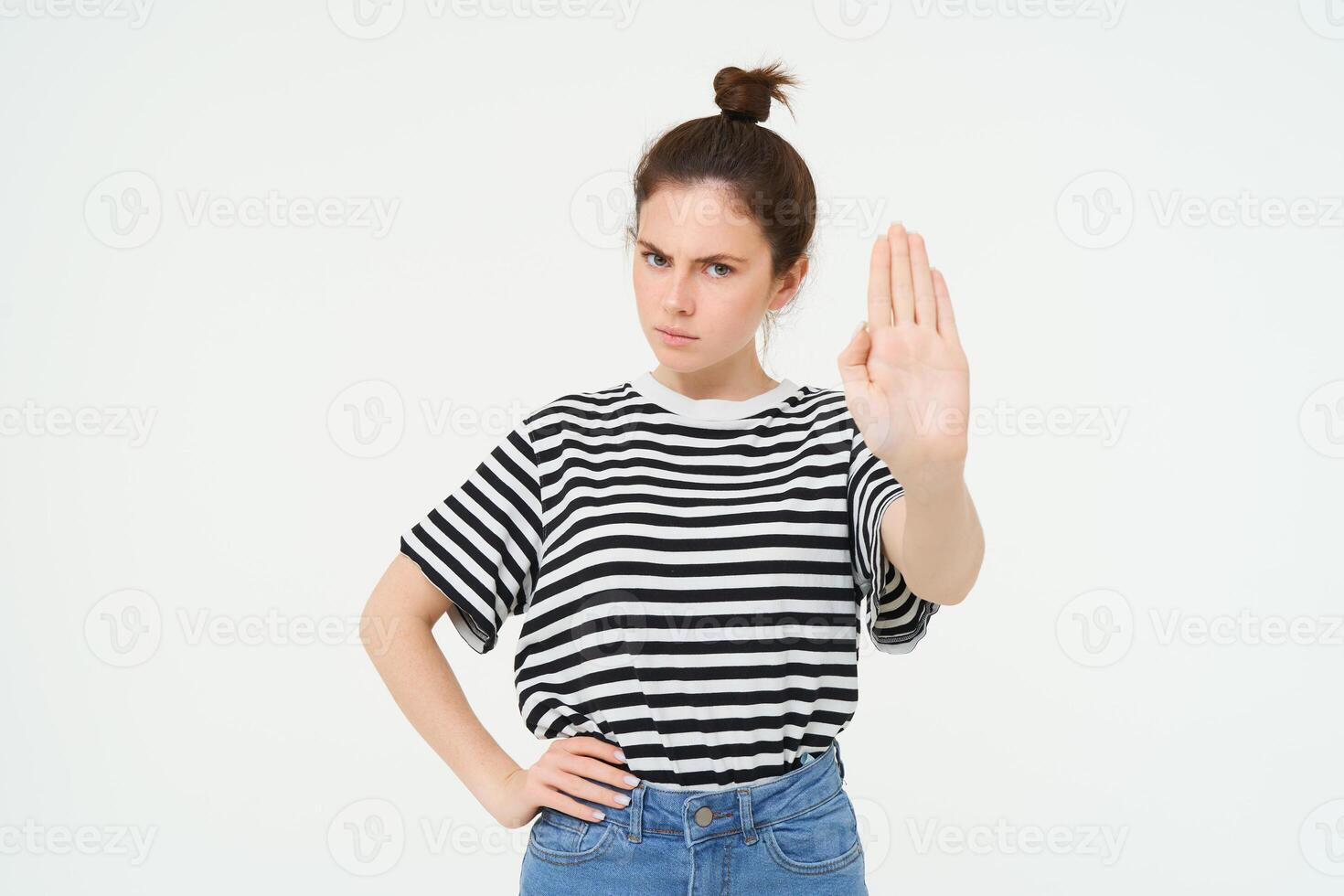 Image of beautiful woman with serious face, showing stop sign, extends one palm and frowns, stands over white background photo