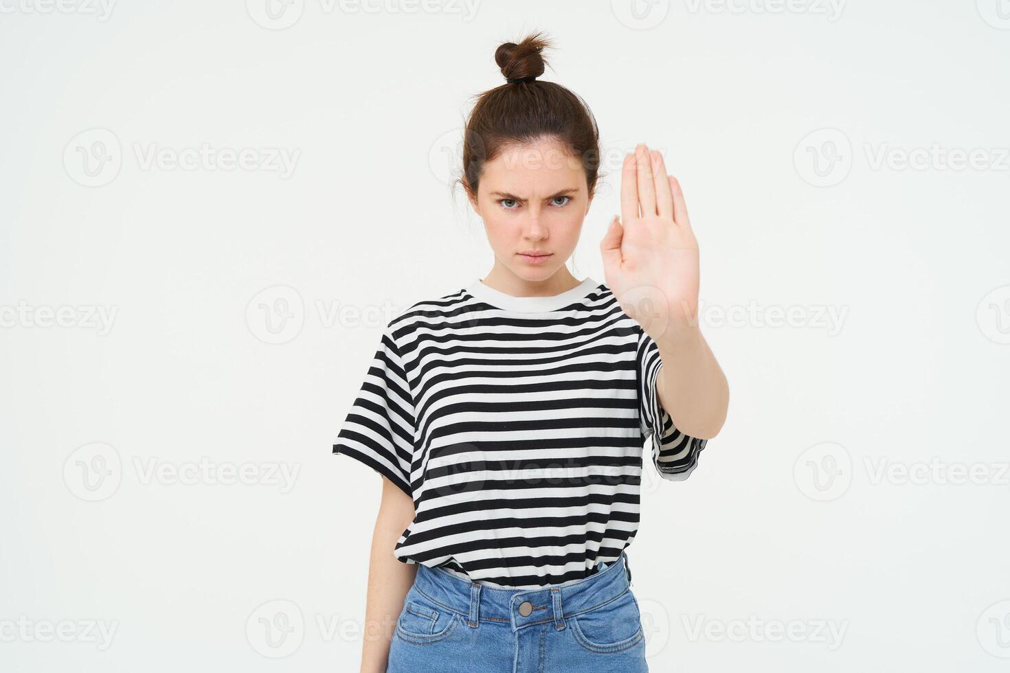 Image of serious and confident young woman, shows stop sign, taboo gesture, prohibit something bad, standing over white background photo