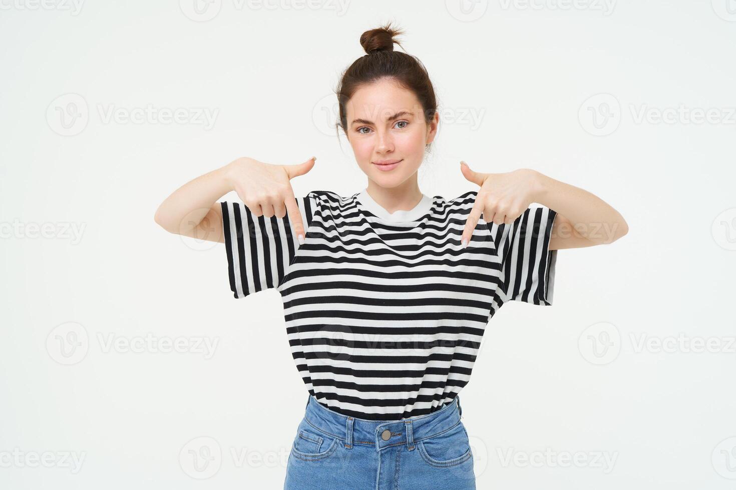 Portrait of confident, smiling brunette woman, pointing fingers down, showing banner on bottom, follow link below gesture, standing over white background photo