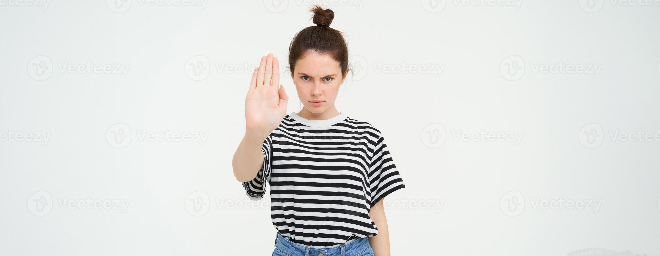 Image of serious and confident young woman, shows stop sign, taboo gesture, prohibit something bad, standing over white background photo