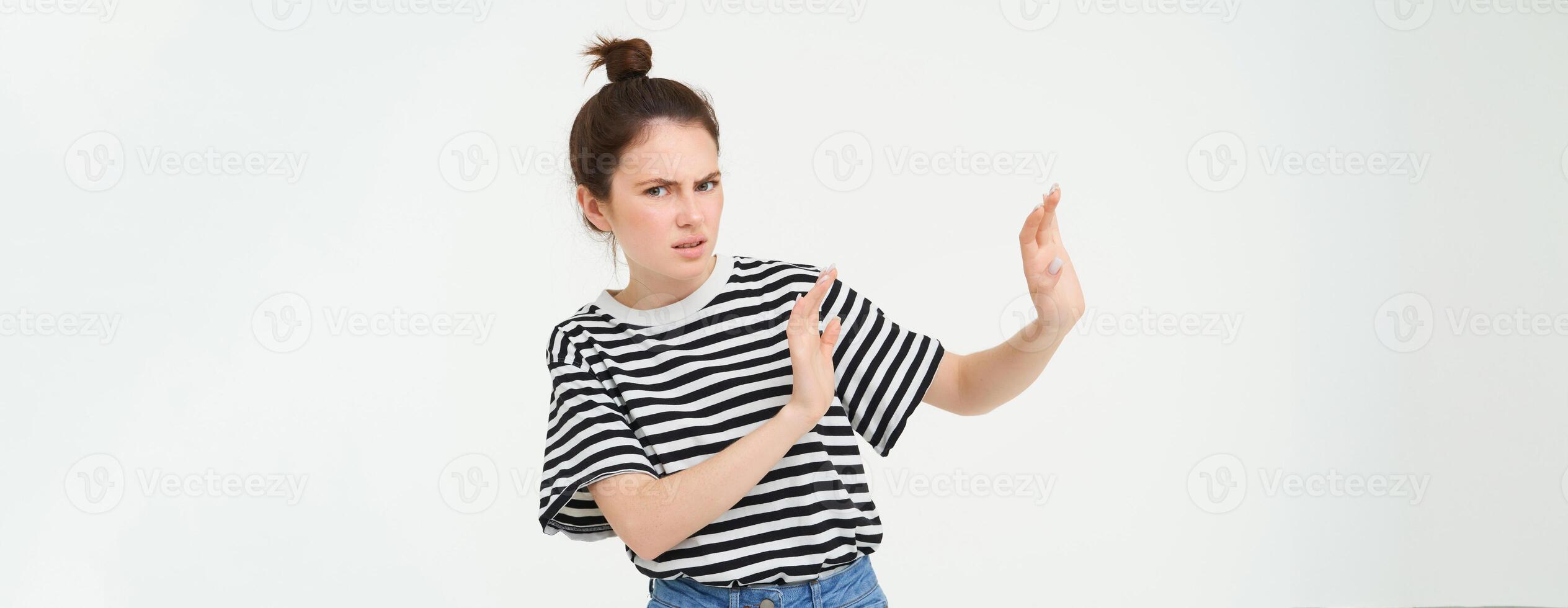 Image of woman expressing aversion, dislike something, looks apalled, extends hands forward in defensive gesture, rejecting, refusing, standing over white background photo