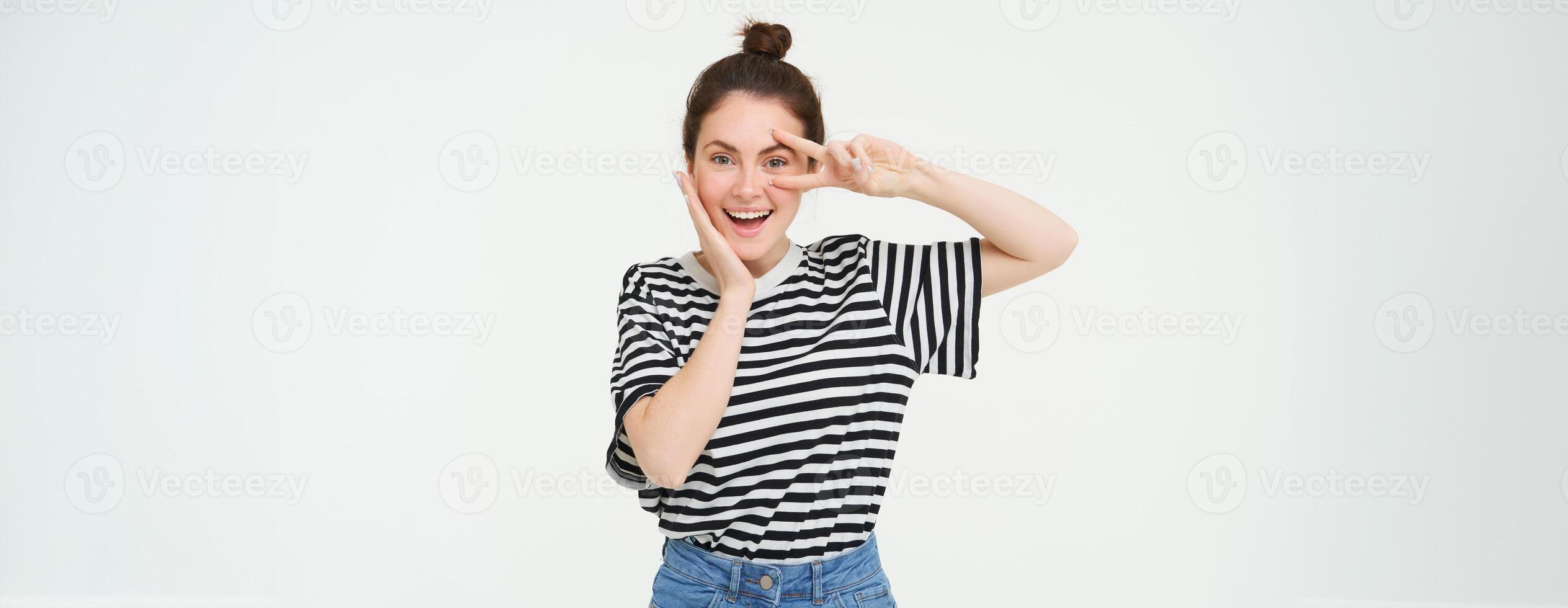 Beautiful brunette woman shows peace sign near eye and smiling, isolated against white background photo