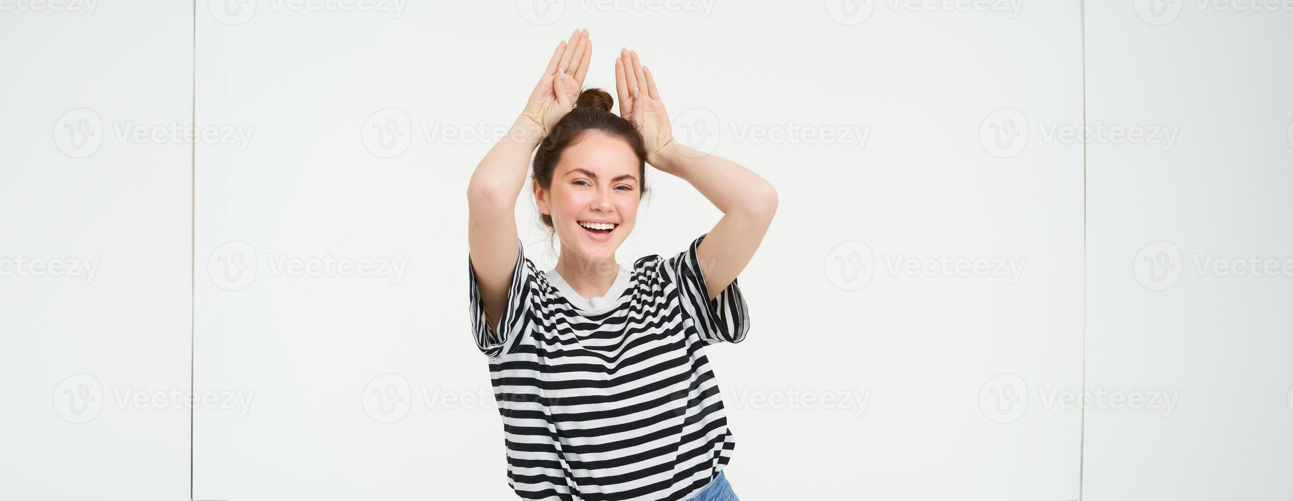 Young woman laughing, showing animal floppy ears gesture with hands on top of head, smiling and looking happy, isolated over white background photo