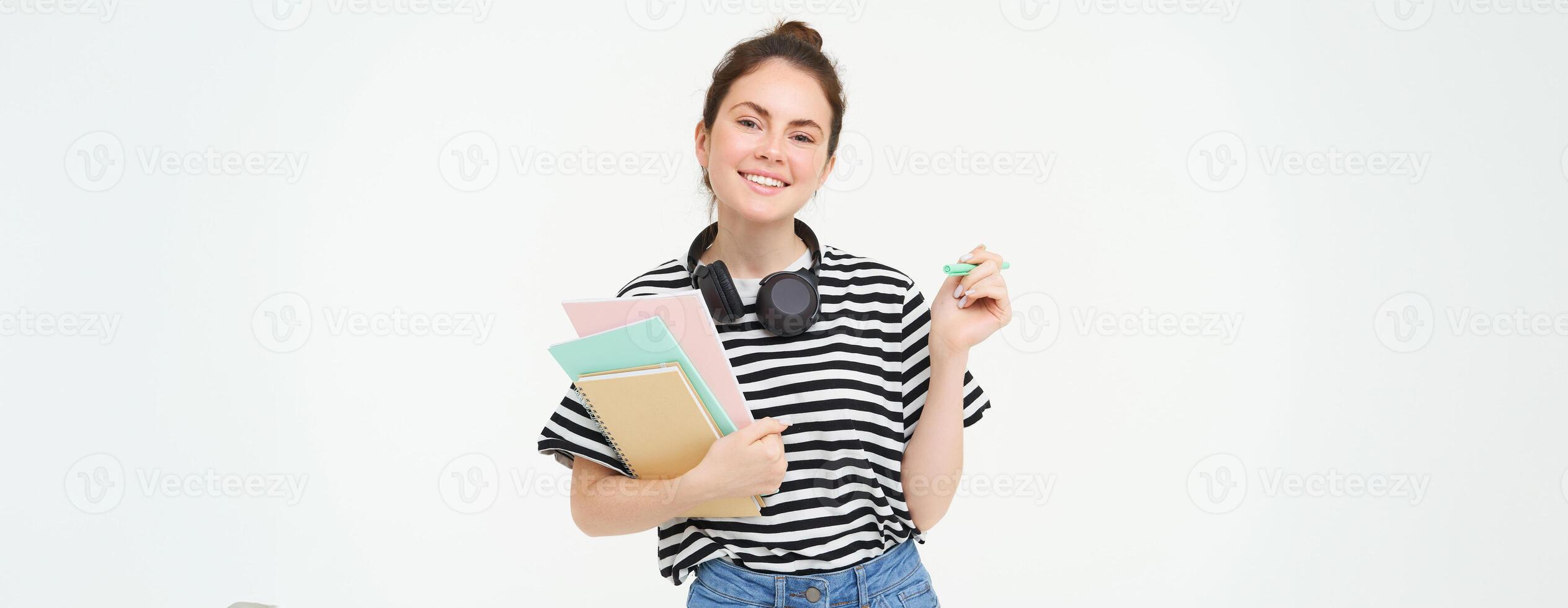 Image of young woman, tutor with books and notebooks, wearing headphones over her neck, isolated on white background. Student lifestyle concept photo