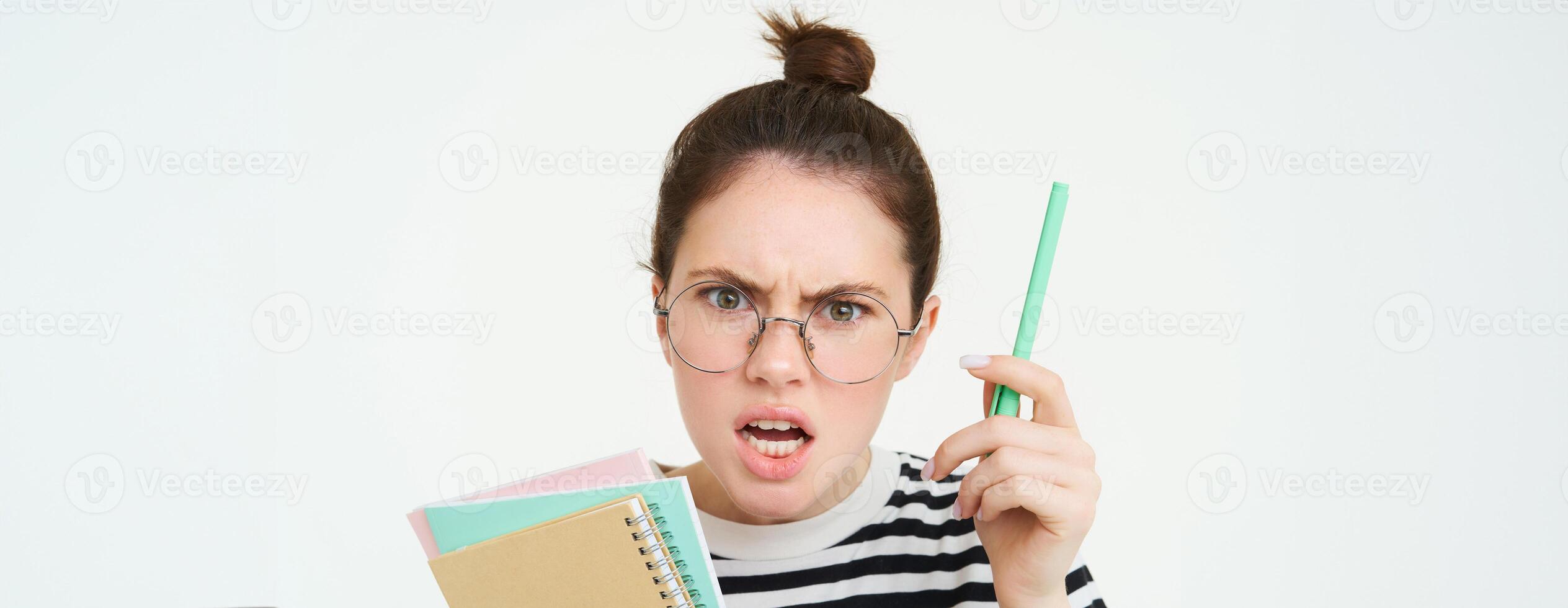 Close up portrait of woman shouting, wearing glasses, shaking pen and holding paperwork, notebooks, teacher arguing, scolding someone, standing over white background photo